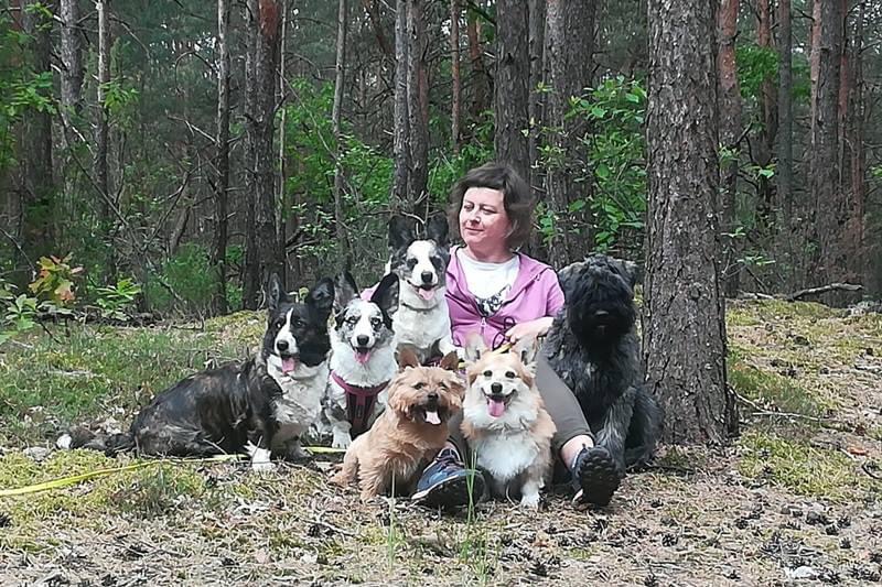 Kobieta siedząca na leśnej ścieżce z psem rasy Welsh Corgi Cardigan, co podkreśla bliską więź i komfortowe momenty spędzane na łonie natury.